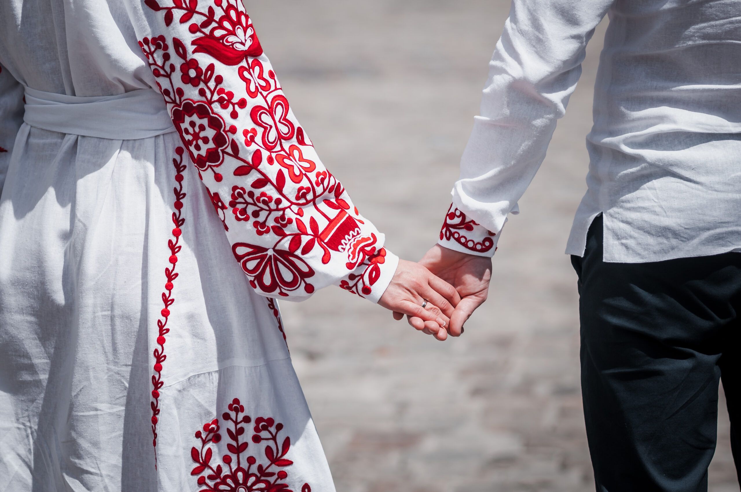 a from-behind shot of newlyweds holding hands, the woman in a dress with red embroidery