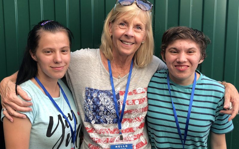 Several young adults and teenagers stand in a kitchen, posing for the camera; one teen kneels down in front